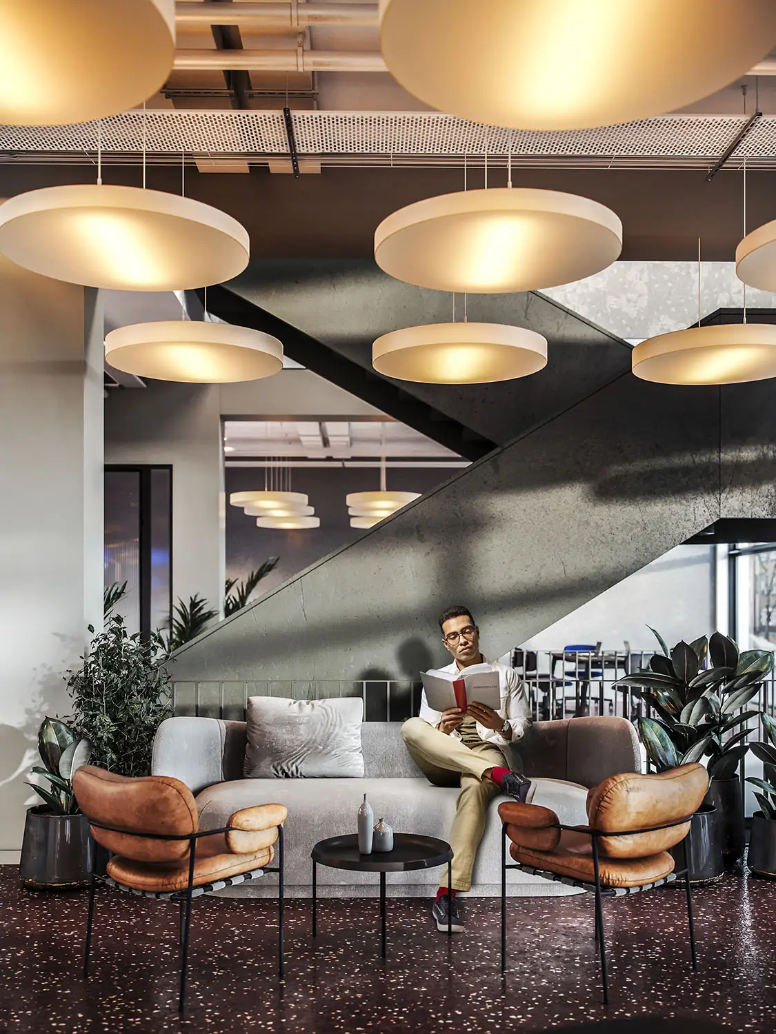 Man reading in a modern lounge area with stylish lighting and comfortable seating.