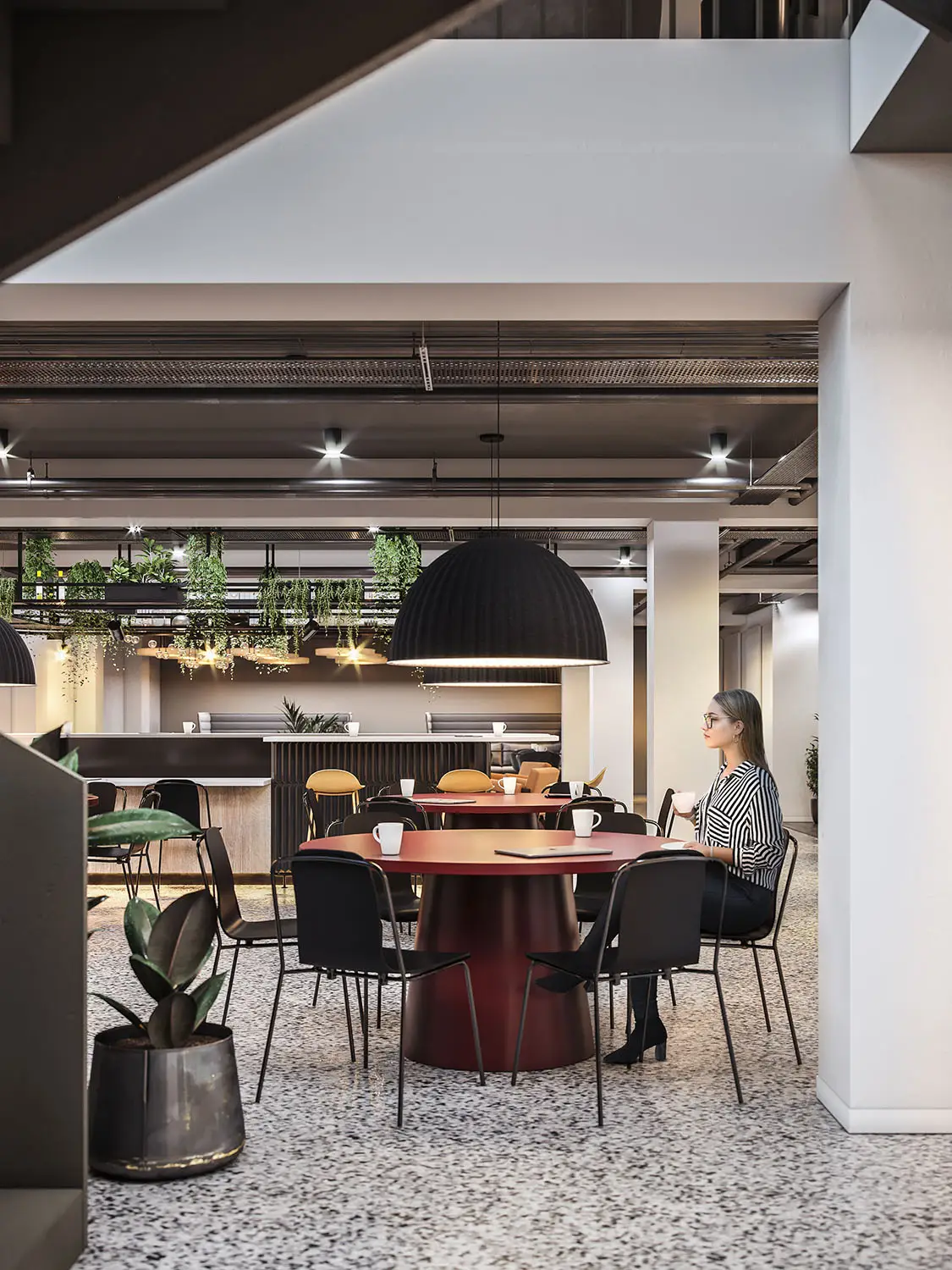 Modern office break area with red table, black chairs, and stylish lighting, woman seated.